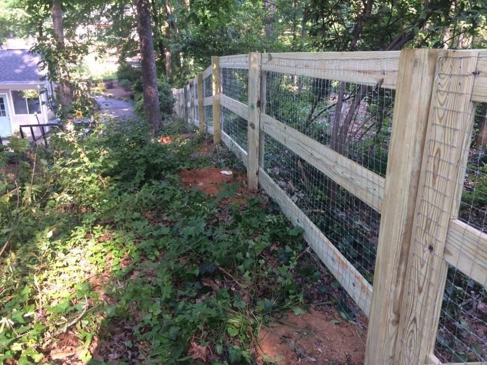 Two-rail wood split rail fence with wire backing on a wooded slope by Advanced Custom Fence in Charlotte, NC